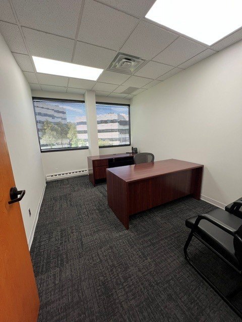 A furnished private office with desk, credenza and a window onto the campus